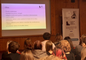 Slajd opisujący warunki życia w obozie dla dzieci oraz roll-up z nazwą i danymi kontaktowymi Muzeum Dzieci Polskich.