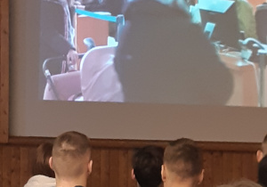 Uczniowie oglądają prezentację, pokazująca różne aktywności funkcjonariuszy – ten slajd pokazuje pracę funkcjonariuszy na lotnisku.